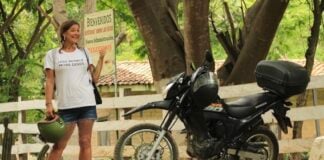 A woman in a white t-shirt stands next to a black touring motorcycle