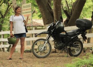 A woman in a white t-shirt stands next to a black touring motorcycle