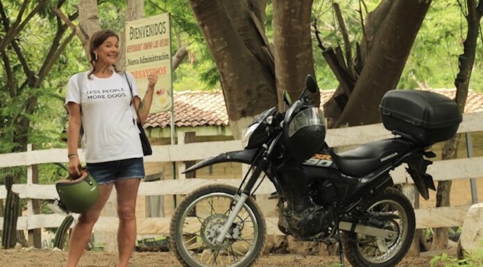 A woman in a white t-shirt stands next to a black touring motorcycle