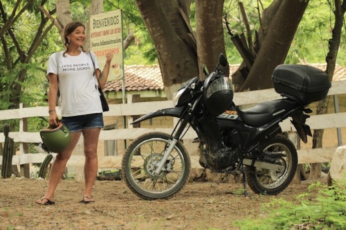 A woman in a white t-shirt stands next to a black touring motorcycle