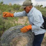 Ejido member in work gloves rolling up a coil of barbed wire that was removed from the Las Margaritas ejido in Wirikuta.