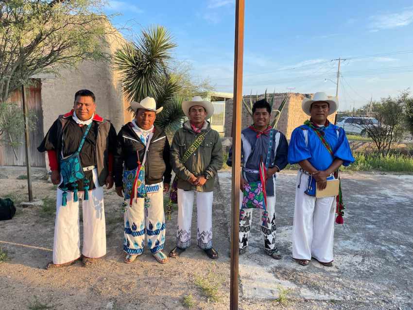 A delegation of five Wixárika men, some wearing traditional embroidered clothing and cowboy hats, standing together at the Ejido Las Margaritas in Las Margaritas, San Luis Potosi, Mexico.
