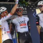 Teammates in cycling gear and helmets places a palm crown on Mexican cyclist Isaac del Toro