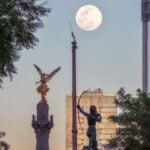 A high up view of the Mexico City Independence Angel and a few of the city's skyscrapers are seen against an afternoon supermoon.
