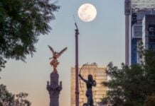 A high up view of the Mexico City Independence Angel and a few of the city's skyscrapers are seen against an afternoon supermoon.