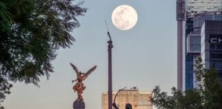 A high up view of the Mexico City Independence Angel and a few of the city's skyscrapers are seen against an afternoon supermoon.