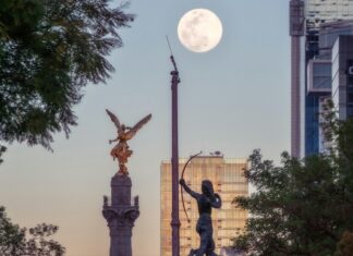 A high up view of the Mexico City Independence Angel and a few of the city's skyscrapers are seen against an afternoon supermoon.