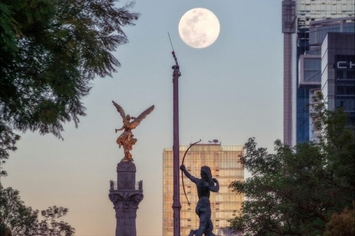A high up view of the Mexico City Independence Angel and a few of the city's skyscrapers are seen against an afternoon supermoon.