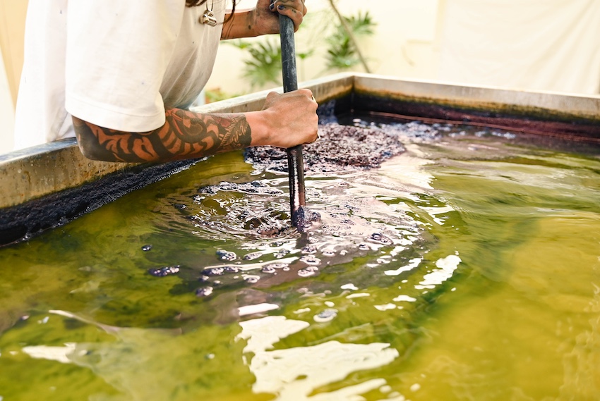 a woman stirring a vat of indigo dye