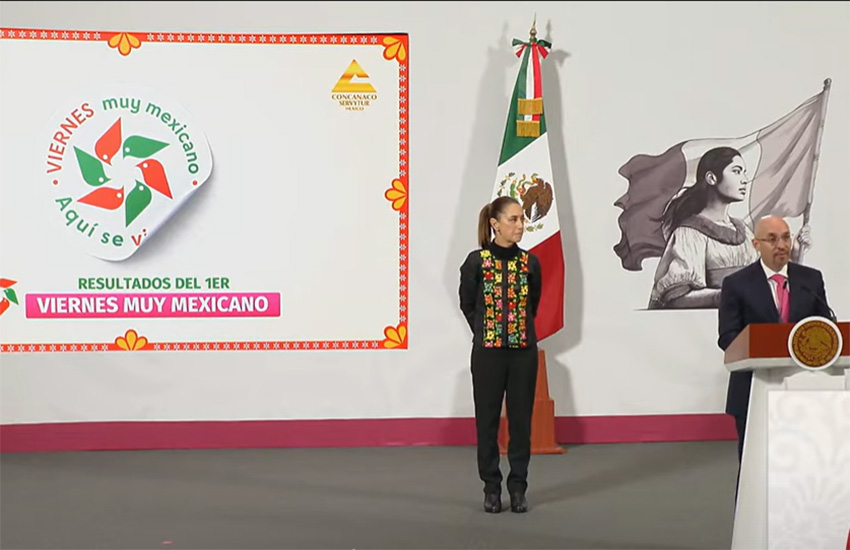 Sheinbaum stands next to a projection of a Viernes Muy Mexicano pinwheel sticker at a press conference