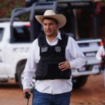 Uruapan Mayor Carlos Manzo in front of a police car wearing a cowboy hat and bullet proof vest