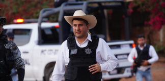 Uruapan Mayor Carlos Manzo in front of a police car wearing a cowboy hat and bullet proof vest