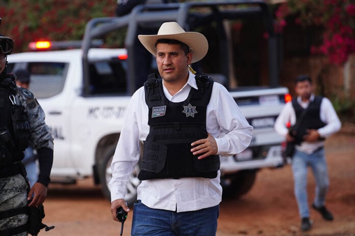 Uruapan Mayor Carlos Manzo in front of a police car wearing a cowboy hat and bullet proof vest