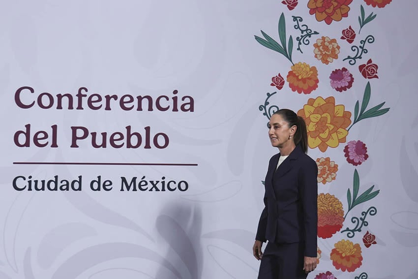 President Sheinbaum walks onto a stage with a banner reading Conferencia del Pueblo, Ciudad de Mexico