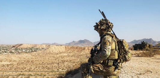 A US soldier in camo surveils a desert valley in New Mexico