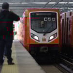 Riders wait as an orange Mexico City Metro train pulls into the station