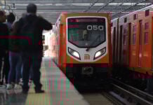 Riders wait as an orange Mexico City Metro train pulls into the station