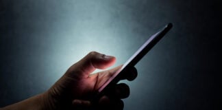 A hand holds a cell phone against a dark background