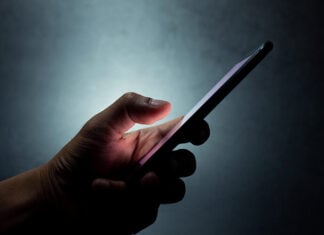 A hand holds a cell phone against a dark background