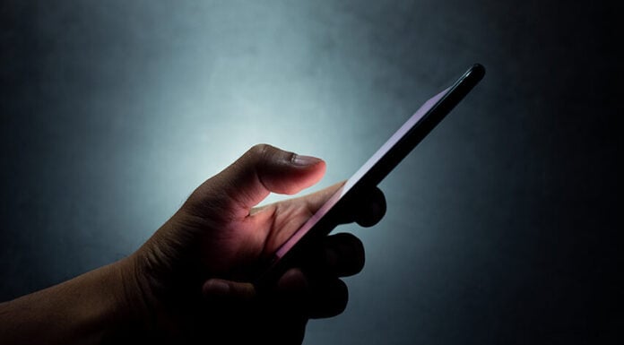 A hand holds a cell phone against a dark background