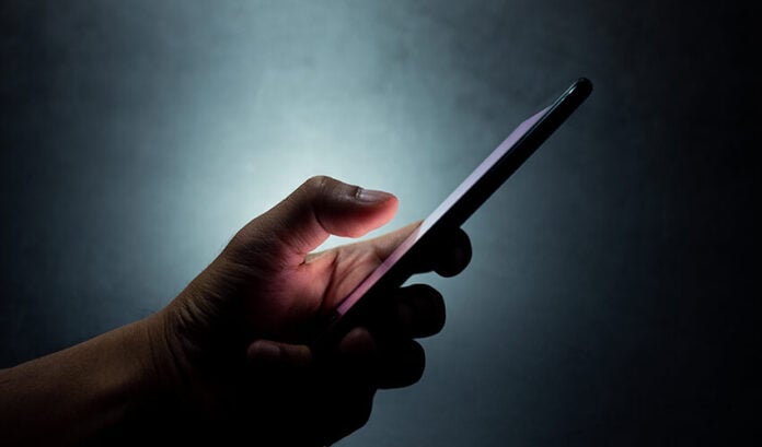 A hand holds a cell phone against a dark background