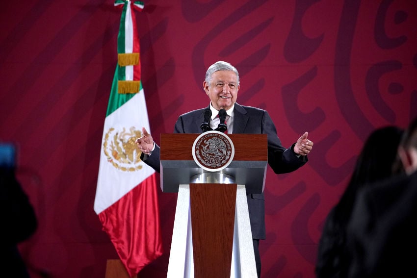 Mexico's former president Andres Manuel Lopez Obrador at a press conference in the presidential palace in Mexico City. He is standing at the presidential podium and speaking to reporters with his arms wide open on either side of him.