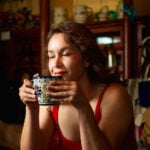 A woman closes her eyes, enjoying the aroma of a traditional Mexican warm drink in a beautiful blue and white Talavera-style ceramic mug.