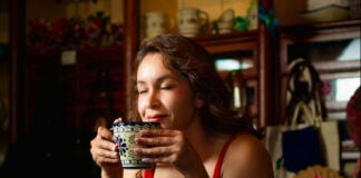 A woman closes her eyes, enjoying the aroma of a traditional Mexican warm drink in a beautiful blue and white Talavera-style ceramic mug.