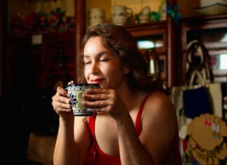 A woman closes her eyes, enjoying the aroma of a traditional Mexican warm drink in a beautiful blue and white Talavera-style ceramic mug.