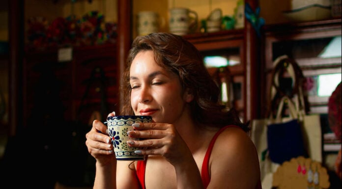 A woman closes her eyes, enjoying the aroma of a traditional Mexican warm drink in a beautiful blue and white Talavera-style ceramic mug.