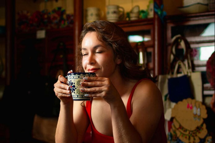 A woman closes her eyes, enjoying the aroma of a traditional Mexican warm drink in a beautiful blue and white Talavera-style ceramic mug.