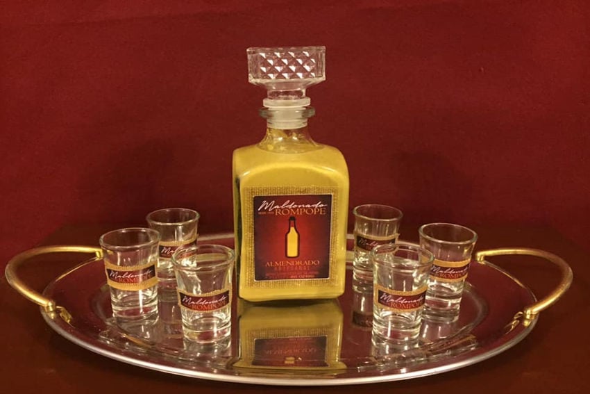 A bottle of creamy yellow, almond-flavored rompope liqueur sits on a silver tray with six shot glasses, representing the commercialized version of this traditional Mexican holiday staple that's often drunk warm during the winter.