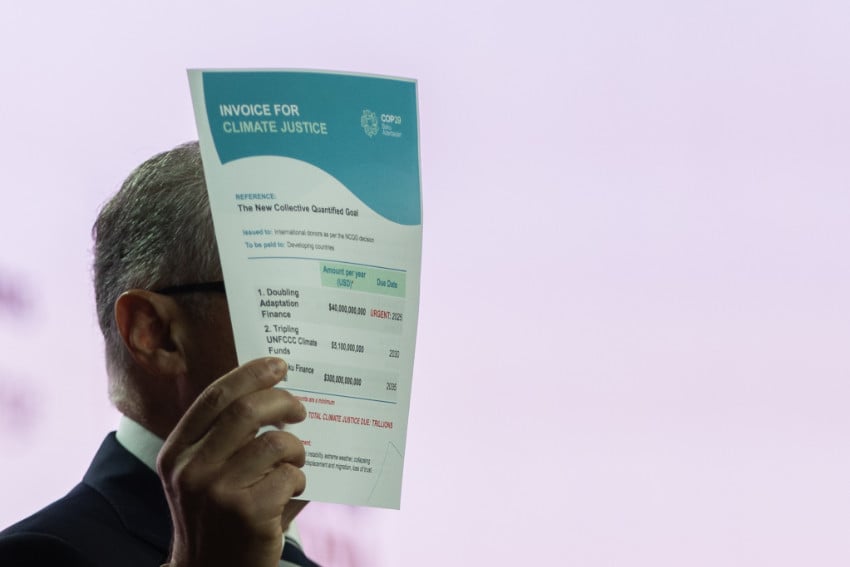 A delegate holds up the "Invoice for Climate Justice" document detailing the New Collective Quantified Goal on climate finance, an international financial mechanism that affects Mexico's climate change commitments for adaptation funding.