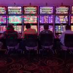 Sillouetted people sit at glowing neon slot machines