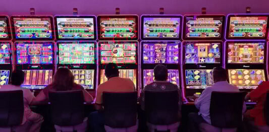 Sillouetted people sit at glowing neon slot machines