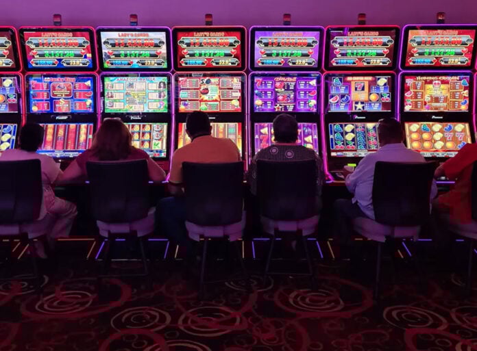 Sillouetted people sit at glowing neon slot machines