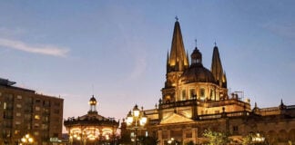 People walk by a Guadalajara cathedral lit up in the evening