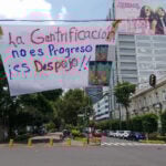 A banner reading "La Gentrificación no es progreso, es despojo" hangs over a Mexico City street