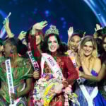 Miss Universe Fatima Bosch waves at the camera while wearing a crown surrounded by other pageant contestants