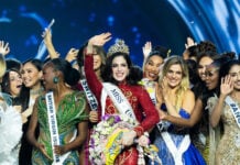Miss Universe Fatima Bosch waves at the camera while wearing a crown surrounded by other pageant contestants