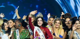 Miss Universe Fatima Bosch waves at the camera while wearing a crown surrounded by other pageant contestants