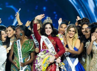 Miss Universe Fatima Bosch waves at the camera while wearing a crown surrounded by other pageant contestants