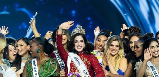 Miss Universe Fatima Bosch waves at the camera while wearing a crown surrounded by other pageant contestants