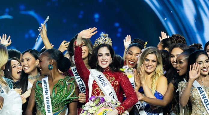 Miss Universe Fatima Bosch waves at the camera while wearing a crown surrounded by other pageant contestants