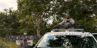 A National Guard truck drives past a sign reading Rancho Sac Lol