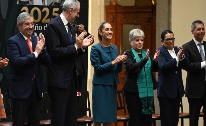President Claudia Sheinbaum stands at the center of a line of Mexican and international delegates at a prepartory meeting for COP30 in Brazil in November. Sheinbaum and the delegates are applauding something while standing on a stage. Behind the people is a black banner that says "2025" and some other words in Spanish that are not visible.