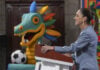 Sheinbaum at a press conference podium in front of a cartoon dragon or maybe quetzalcoatl with a soccer ball