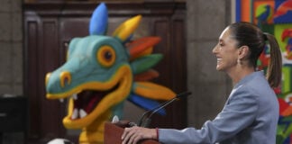 Sheinbaum at a press conference podium in front of a cartoon dragon or maybe quetzalcoatl with a soccer ball