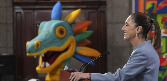 Sheinbaum at a press conference podium in front of a cartoon dragon or maybe quetzalcoatl with a soccer ball
