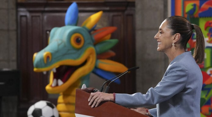 Sheinbaum at a press conference podium in front of a cartoon dragon or maybe quetzalcoatl with a soccer ball